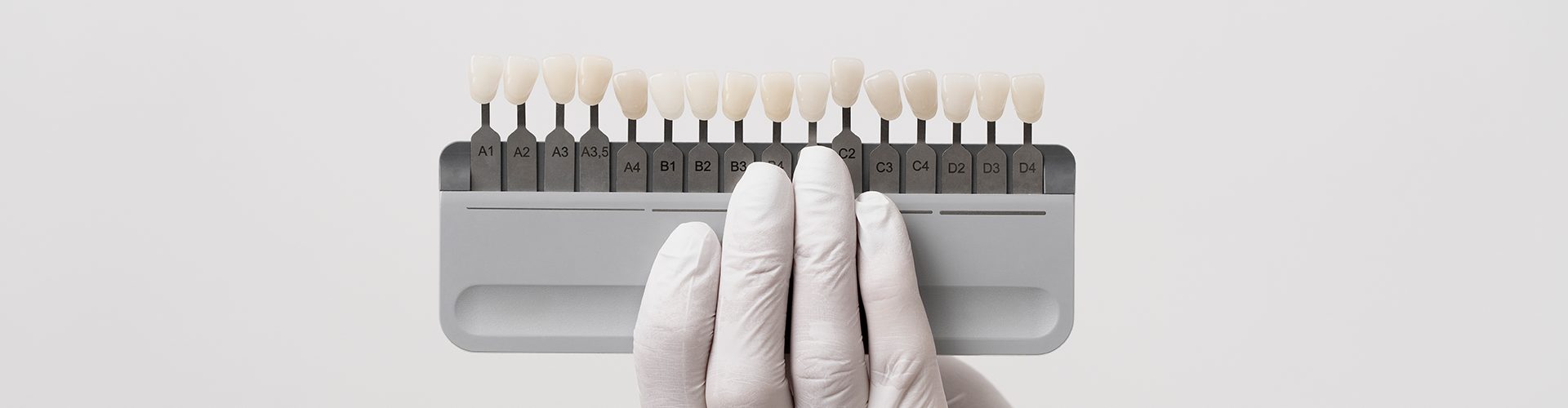 Gloved hand holding tooth shade-matching tool.